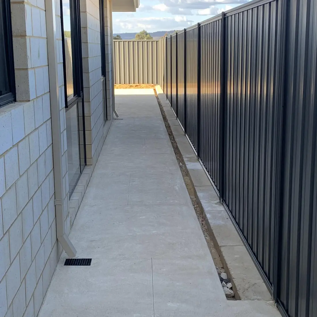 Charcoal Colorbond fence running beside a new concrete side path