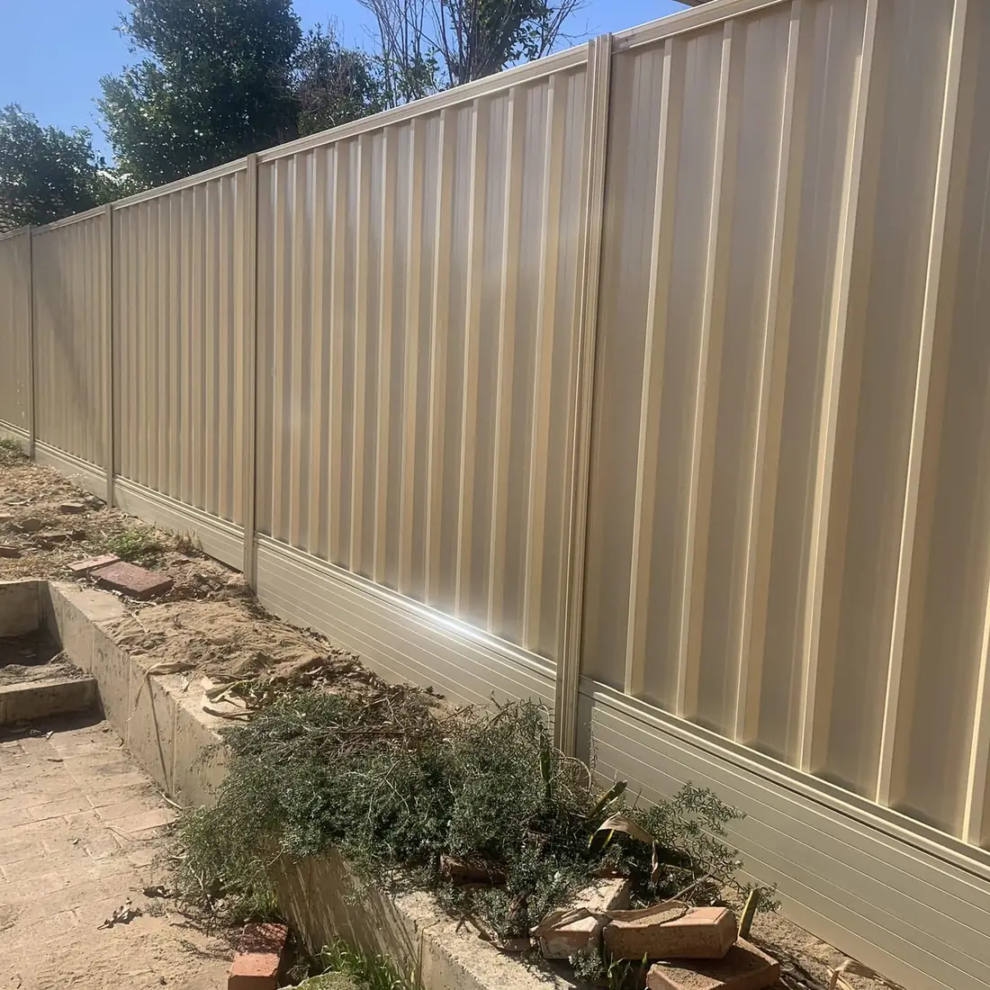 Cream Colorbond fence on a base plinth above a sandy garden bed