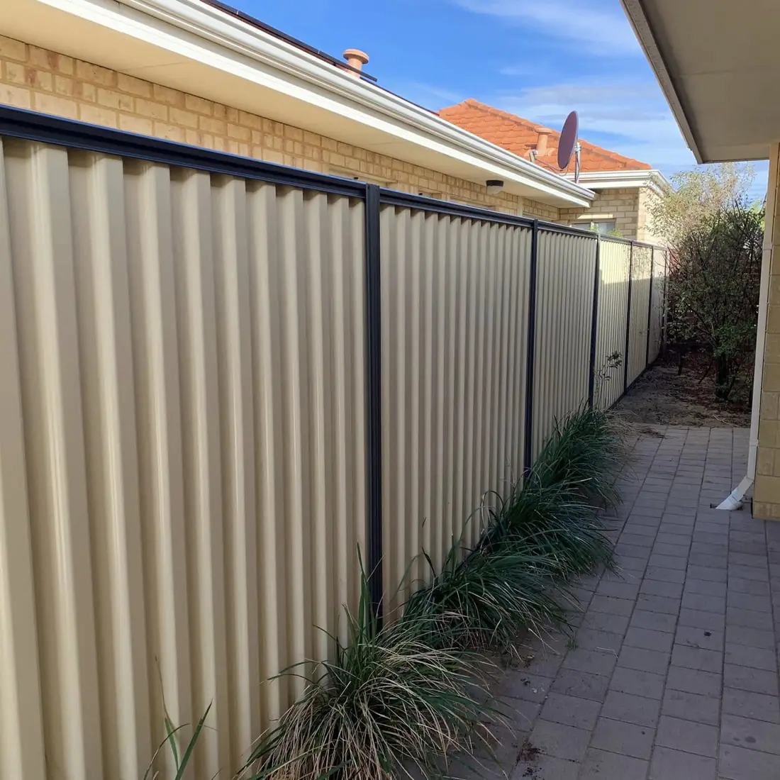 Cream Colorbond fence with dark posts beside a brick paved side path
