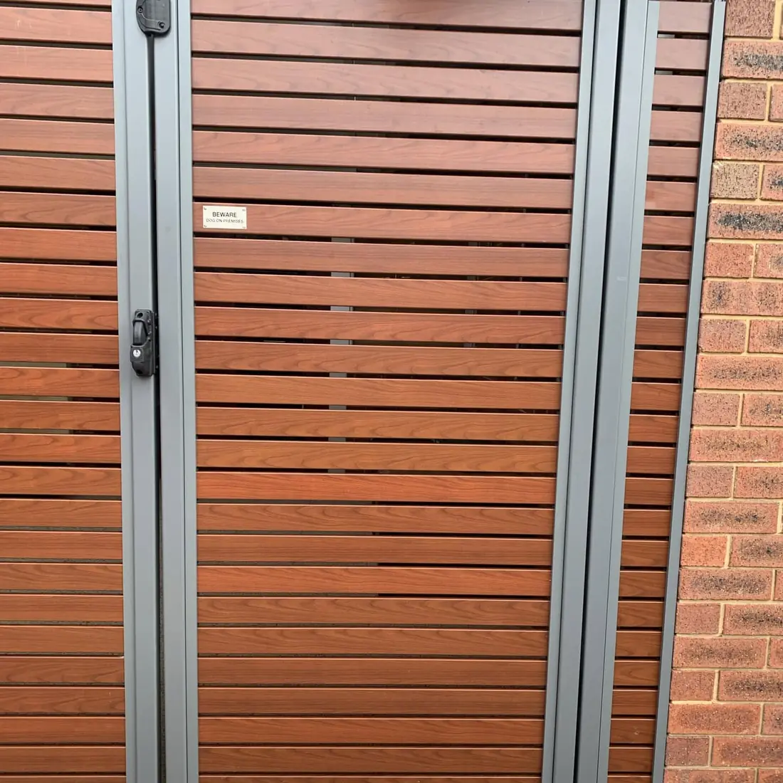 Timber-look slat gate with a grey aluminium frame set in a brick wall